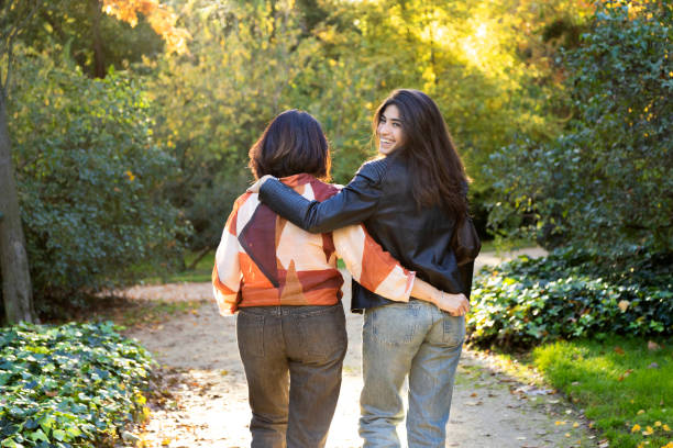 istock Daughter smiles while walking arm-in-arm with her mother on a sunlit park path. 2171454406