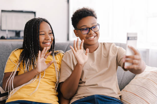 istock Two smiling kids waving during video call at home 2171457074