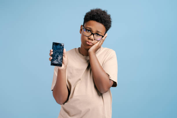 istock Child boy looking worried touching face while holding a broken screen smartphone 2171458022