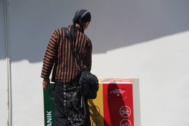 Yogyakarta, Indonesia, August 17, 2024; An adult Indonesian man in traditional dress disposes of trash in a garbage bin