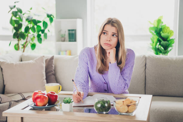 istock Photo of nice young girl sit couch table write notebook look sad empty space wear violet clothes modern cozy interior flat indoors 2171467595