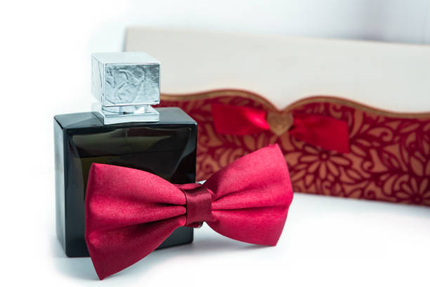 A stylish black perfume bottle lies beside a red bow tie and a beautifully decorated gift box, creating a refined display.