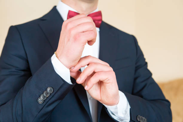 A well-dressed man in a tuxedo adjusts his cufflinks, preparing for an elegant event.