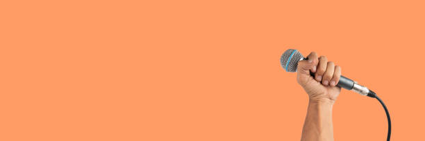 istock Black male hand holding a microphone isolated on orange background banner 2171475862