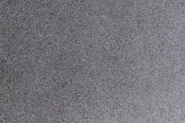 A rough, granular grey surface, reminiscent of coarse sandpaper or asphalt texture. Background