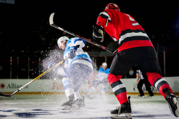 A dynamic shot of ice hockey players in action A dynamic shot of ice hockey players in action, with one player in red and another in blue creating an intense spray of ice as they maneuver on the rink during a fast-paced game. red hockey jersey stock pictures, royalty-free photos & images