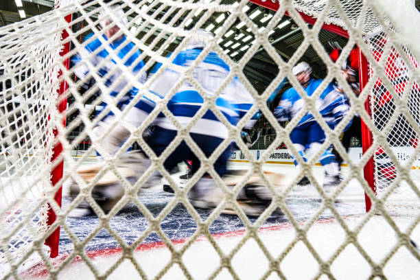 From behind the net, the blurred figures of blue-uniformed ice hockey players rushed around the goal, their intense battle causing the goalkeeper to defend against a barrage of hits.