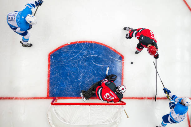 Overhead View of Ice Hockey Players Battling Near the Goal An overhead shot of ice hockey players in red and blue uniforms competing for the puck in front of the goal, with the goalie crouched and ready to defend against an approaching attack. red hockey jersey stock pictures, royalty-free photos & images