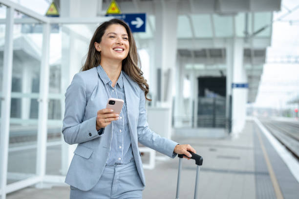 istock Elegant business woman is pulling a suitcase and using the phone at the train station 2171483434