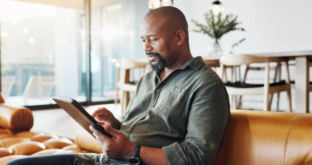 istock Home, tablet and old man on sofa, typing and internet with connection, website info or digital app. African person, apartment or guy with tech, research for insurance policy or email with online news 2171484895