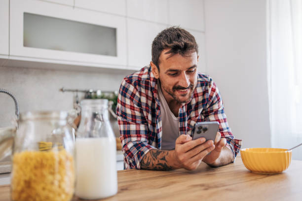 istock An adult man eating cornflakes for breakfast in the kitchen and using smartphone. 2171487496