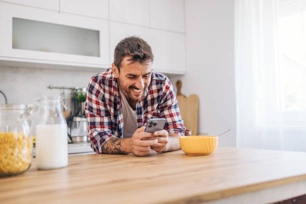 istock An adult man eating cornflakes for breakfast in the kitchen and using smartphone. 2171487569