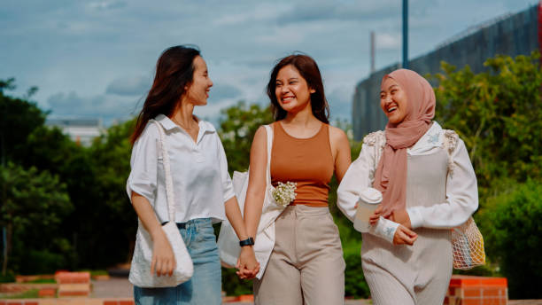 istock Three diverse women walking arm in arm on a park path, laughing and enjoying a fun and carefree moment together on a sunny day. 2171491272