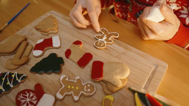 Woman Adds Final Touches to a Gingerbread Man Cookie, Surrounded by Colorfully Decorated Christmas Cookies on a Wooden Board.