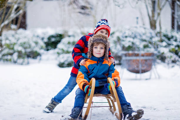 Two kid boys having fun sleigh ride during snowfall. Children sledding on snow. siblings riding a sledge. Twins play outdoors. Friends sled in snowy winter park. Active fun for family vacation.