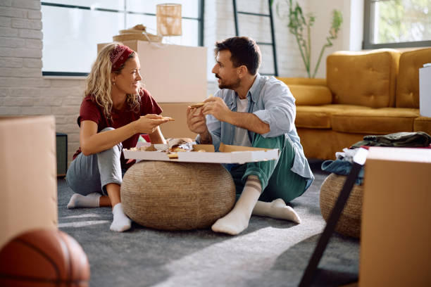 Smiling couple talking while eating pizza in their new apartment.