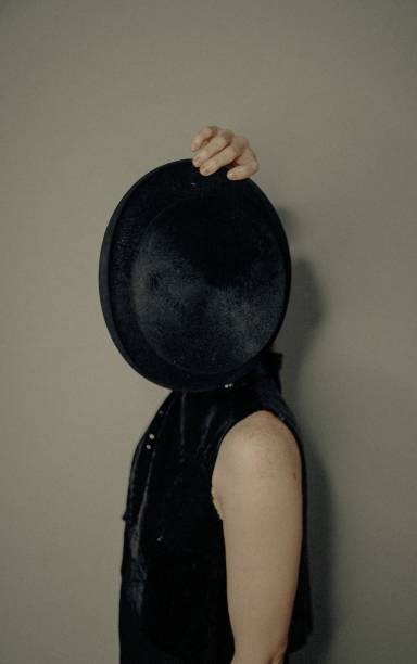 Photo of a woman with an old top hat. She is covering her face with her hat.