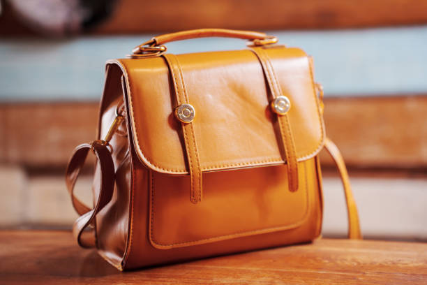 A brown leather bag with a handle and a long strap. It is sitting on a wooden table.