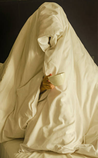 istock a person wrapped entirely in a blanket, resembling a ghost, holding a cup 2171517653