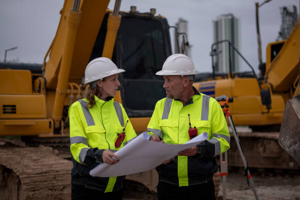 istock Construction workers are standing in front of heavy machinery (an excavator) and examining a large blueprint or construction plandiscussing the project details concept. 2171518731