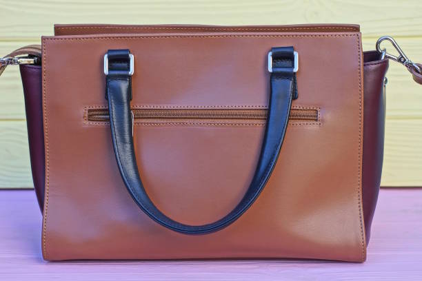 one big brown leather bag with black handle stands on pink table against yellow wall