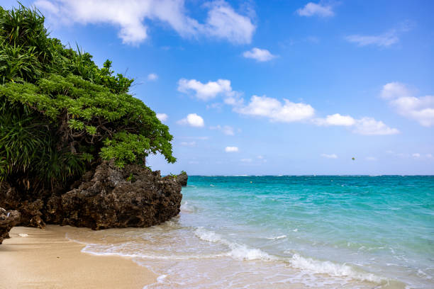Tropical beach with soft sand, turquoise water, and a rocky coastline under a partly cloudy sky