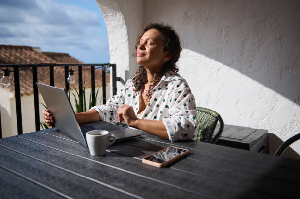 istock Woman enjoys sunlight on balcony while working on laptop, feeling relaxed and peaceful during a remote work day 2171531516