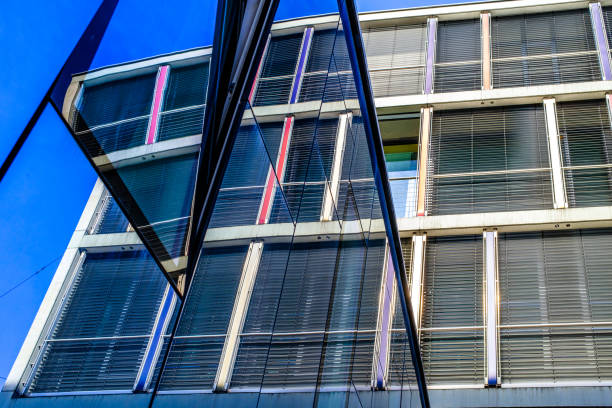 Diagonal close-up of a modern glass building facade, showing repeating vertical strips of green-tinted windows framed by pale metal, creating a strong geometric pattern.