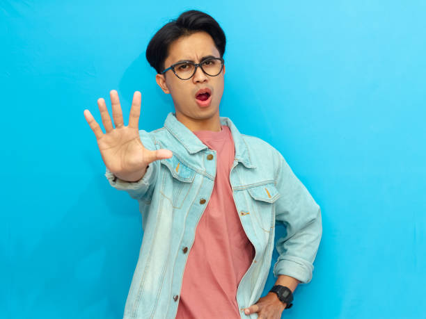 istock Angry Asian man in a denim jacket making a stop gesture with his hand, isolated on a blue background. 2171603583