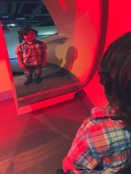 A boy stares curiously at his reflection in a funhouse mirror.