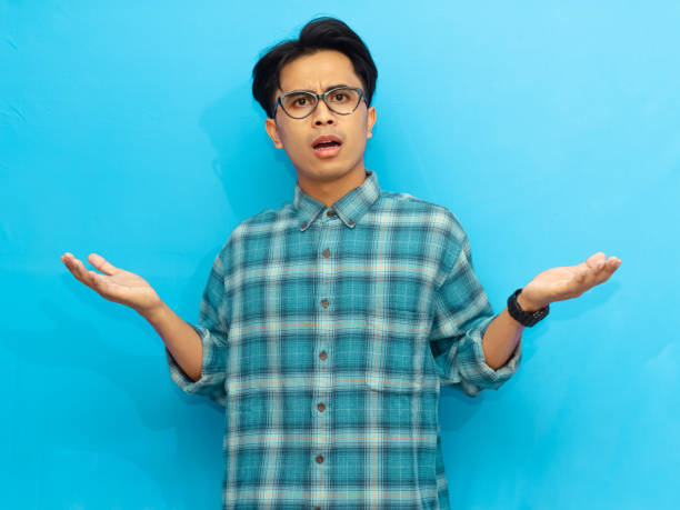 istock Young Asian man wearing casual clothes raises both hands with a confused shocked expression, isolated on a blue background. Perfect for advertisements, promotions, and digital content. 2171603934