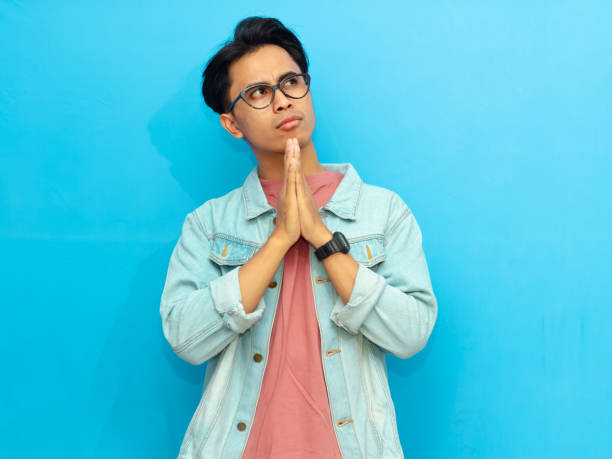 istock Young Asian man in casual clothing posing with a serious expression thinking while looking up isolated on a blue background. Perfect for advertising or promotional content. 2171604267