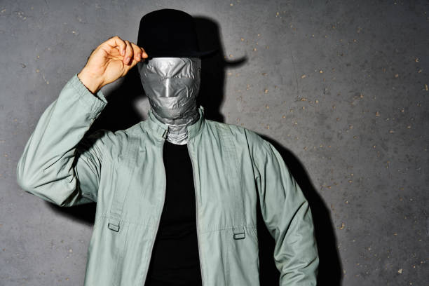 Mystery man with duct tape face greets by raising his hat over gray background