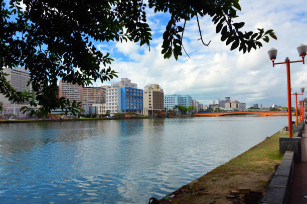 Recife, Pernambuco, Brazil: Capibaribe River and buildings along Sol Street, in the background the Duarte Coelho Bridge (aka Maxambomba Bridge) connecting the neighborhoods of Boa Vista and Santo Antônio, linking two of the city's main avenues: Conde da Boa Vista Avenue and Guararapes Avenue. In the center the headquarters of the Pernambuco Public Prosecutor (PGE) and the Correios building, the state-owned company that operates the national postal service.