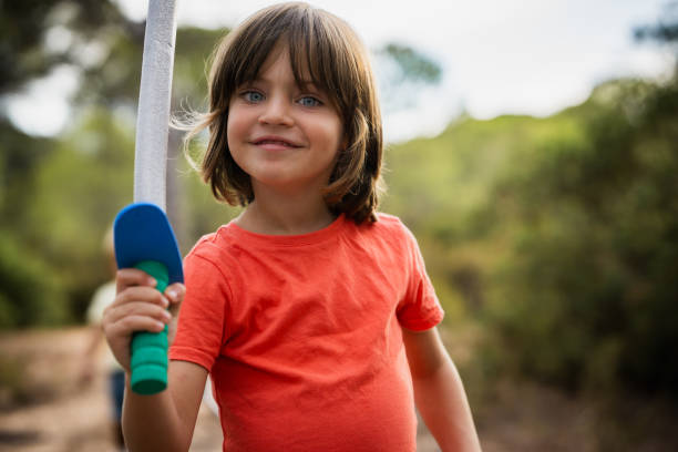 Young boy is holding a toy sword and smiling in a forest