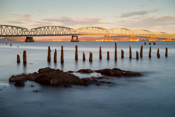 The misty long-exposure waters running through the rock formations in the foreground and the abandoned wooden posts from a discontinued pier bring mystery and history to the scenery.  The beautiful repetitive arches of the Washington end of the bridge are illuminated by a setting sun, as the sky is warm and colorful in the distance.