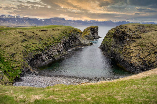 istock Arnarstapi Iceland. Wild coastal cliffs and snowy mountains in the background, against a cloudy sky at sunset 2171620841