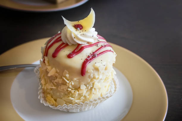 Fine round mini biscuit cake with marzipan, almonds and cream, decorated with red icing on a plate and a dark brown table, festive dessert for holiday celebration, copy space, selected focus