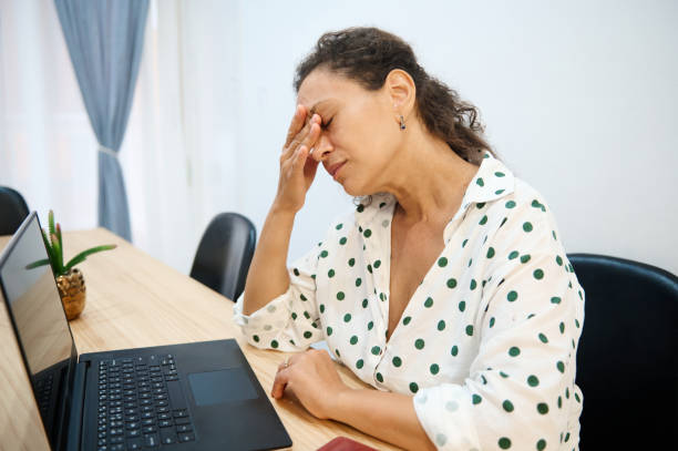 istock Exhausted woman with a headache sitting at desk, stressed and tired from work, using a laptop in a home office environment 2171622991