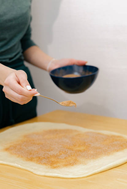 One Caucasian young girl sprinkles cinnamon sugar on the dough on the table.
