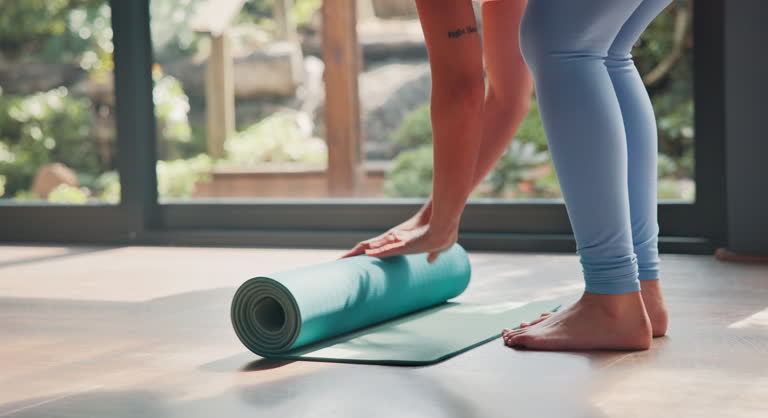 Woman, legs and yoga with mat on floor for pialtes, exercise or indoor workout at home. Female person, hands or yogi rolling training mat for start, warm up or getting ready to stretch at health club