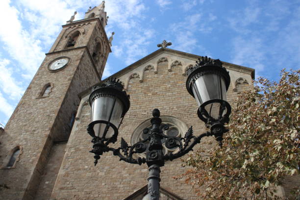 It's a church with a clock tower in it's right side. In front of the church there is a black lamp post and a part of a tree in the left corner of the picture. The sky is very blue but with some clouds in it.