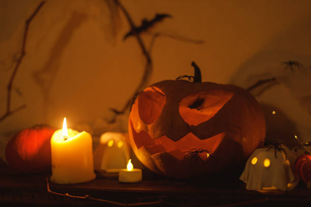 istock Happy Halloween! Spooky Jack o lantern pumpkin, glowing ghosts, spiders and bats in dark. Atmospheric halloween decor on table. Trick or treat 2171643340