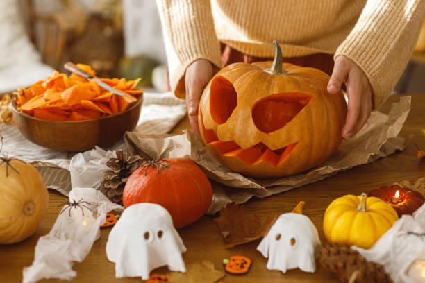 istock Making jack o lantern. Woman carving halloween pumpkin on table with ghosts and spiders, halloween preparation. Making halloween decorations 2171643725