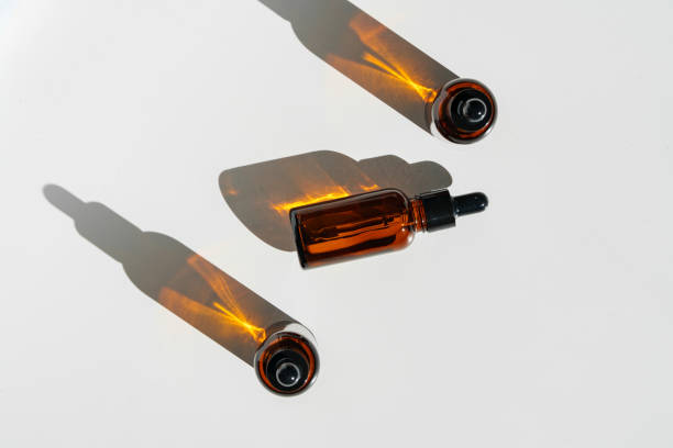 istock Arranged Amber Glass Bottles With Droppers on White Surface Accentuated by Shadows in Bright Light 2171654699