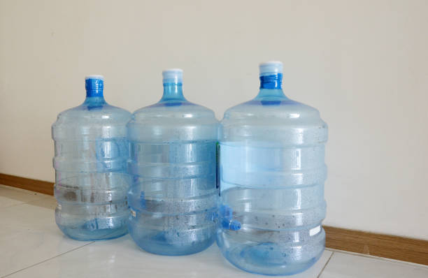 Empty used plastic water cooler bottles line up on the floor