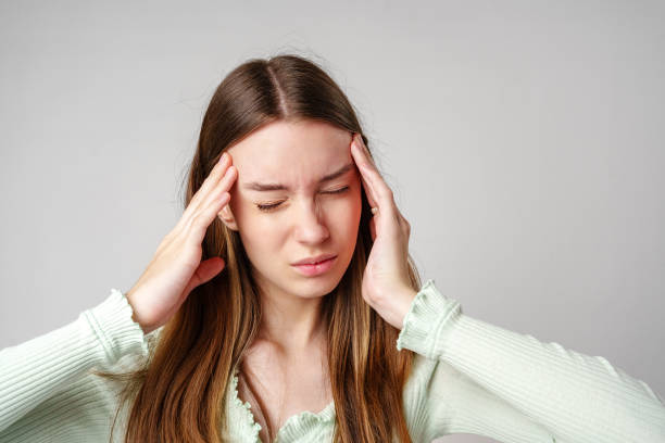 istock Woman Experiencing a Headache Holding Her Temples Against a Grey Background 2171660590