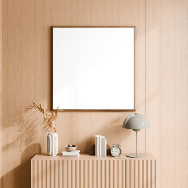 istock Modern minimalist setup featuring a wooden console table adorned with a white vase, dried plants, books, a grey lamp, an alarm clock, and a blank square picture frame. 3d render. 2171660680