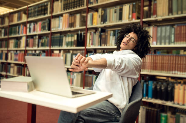 istock Young man sitting at the laptop in the library and looking tired 2171663990