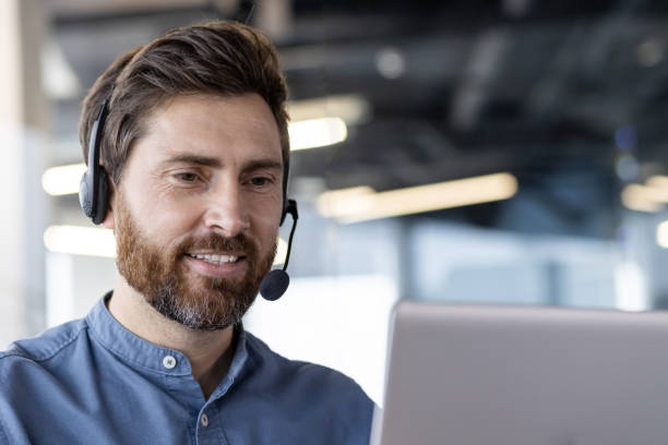 istock Smiling businessman with headset working on laptop in modern office setting 2171671306